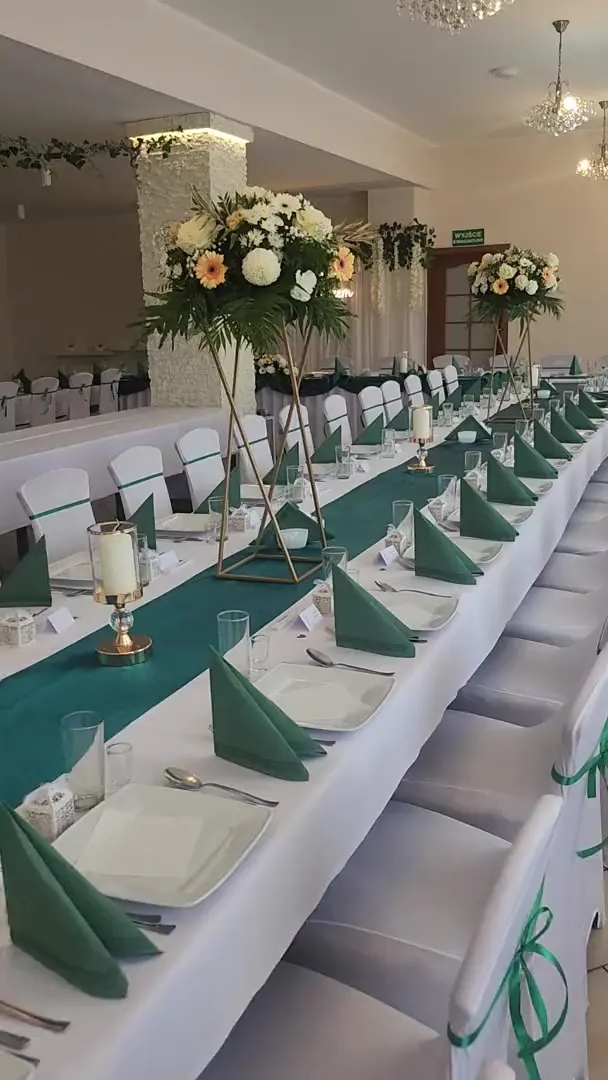 Sala z długim stołem i wysokimi kompozycjami kwiatowymi